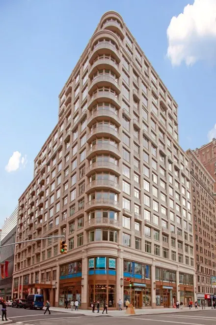 Tall beige corner high-rise building with rounded balconies on a city street under a blue sky