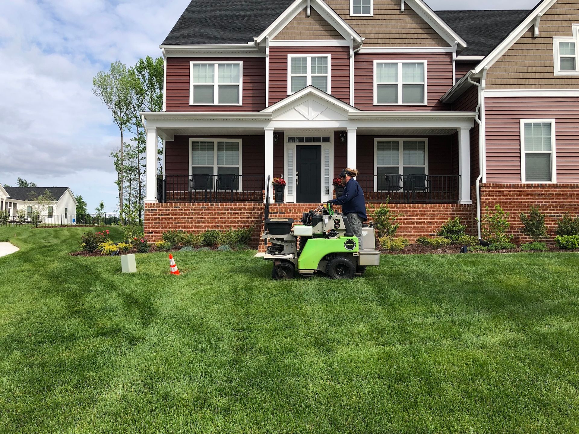 A man is riding a lawn mower in front of a large house.