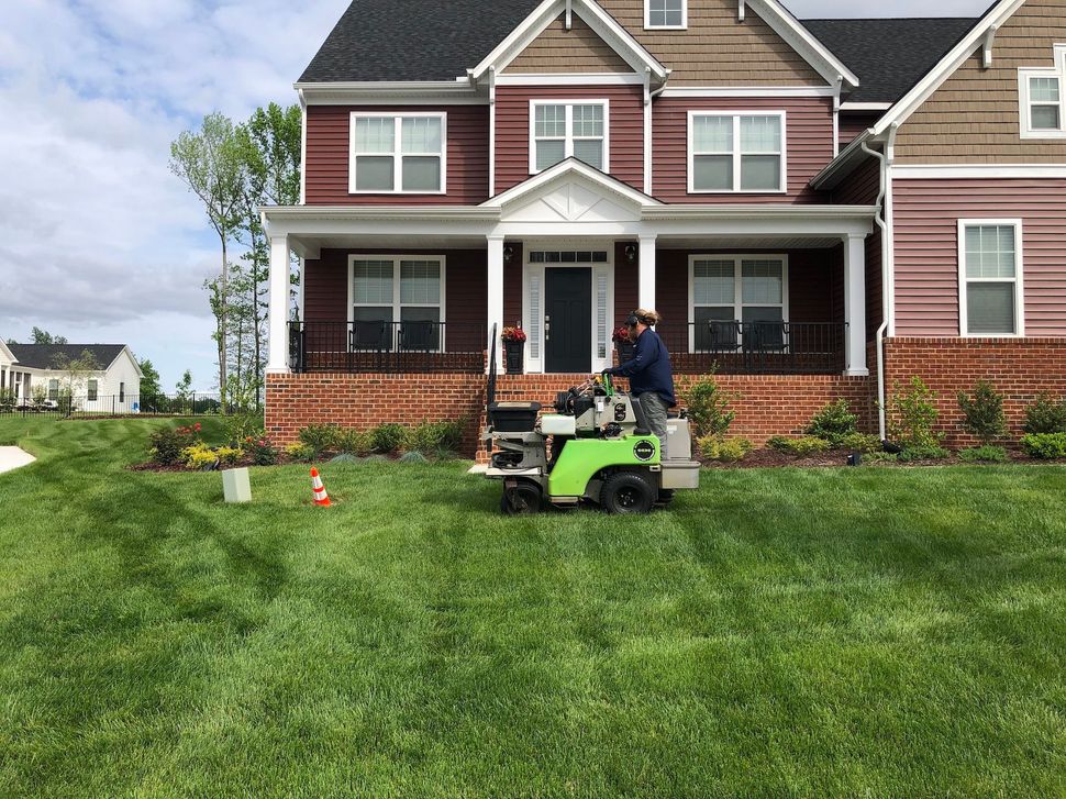 A man is riding a lawn mower in front of a large house.