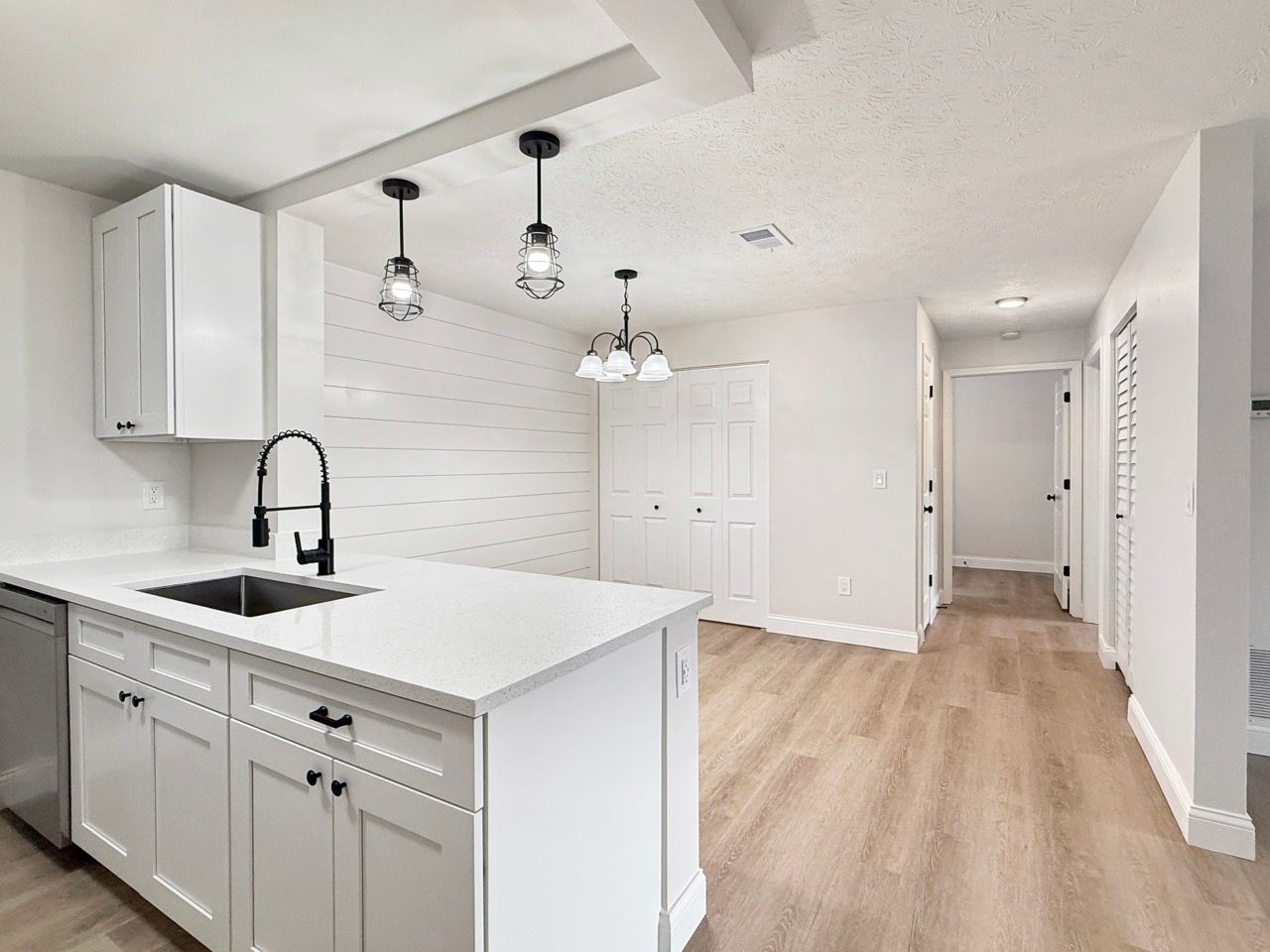 Bright white kitchen with island, pendant lights, and light wood floors in an open hallway space