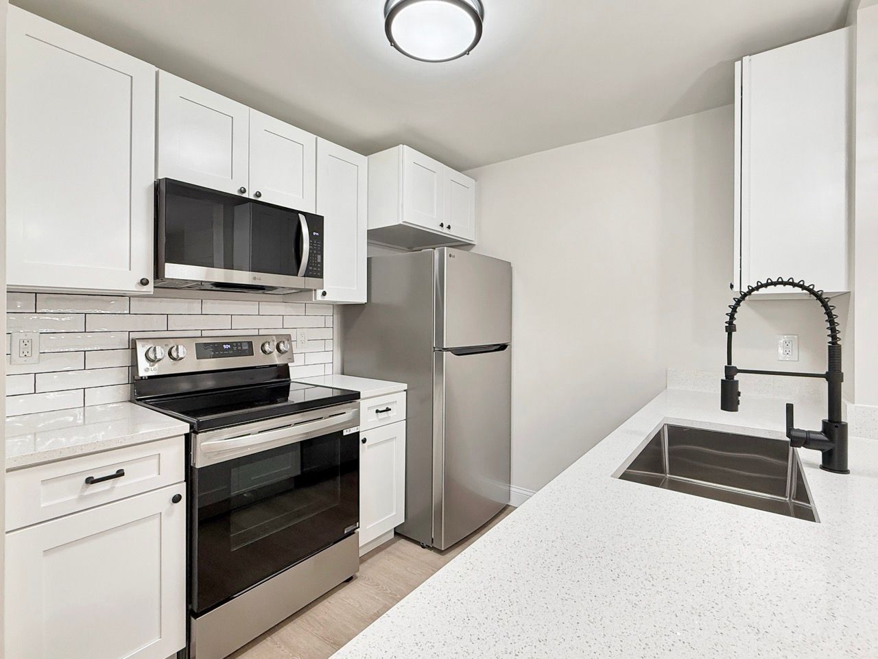 Bright white kitchen with stainless appliances, black oven and sink, and speckled countertop