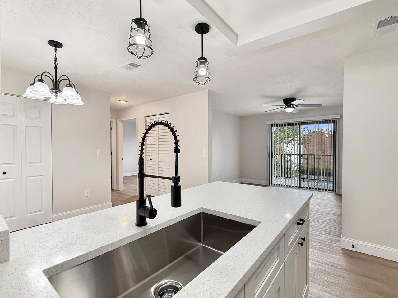 Bright kitchen with white countertops, stainless sink, black faucet, pendant lights, and sliding glass door.