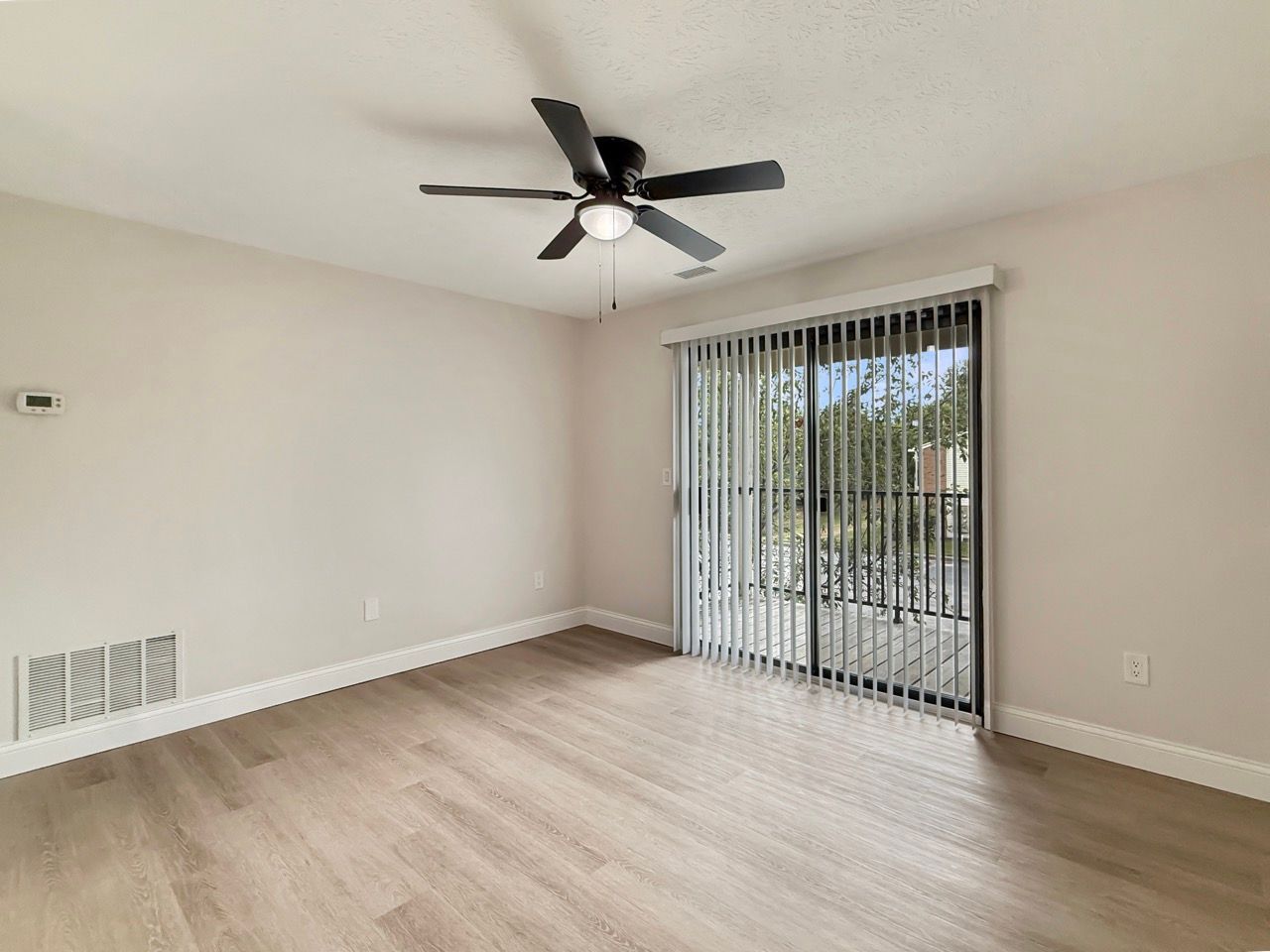 Empty beige living room with ceiling fan and sliding glass door with vertical blinds