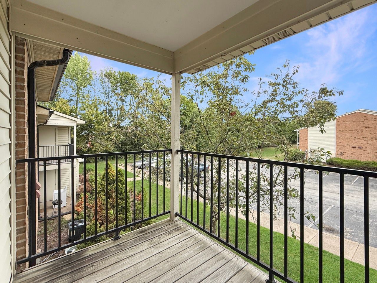 Covered balcony with black railing overlooking a grassy courtyard and residential street.