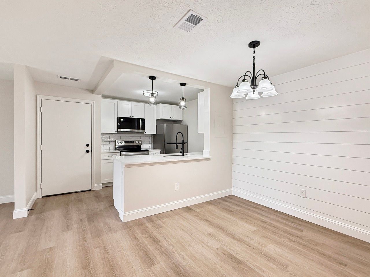 Empty open-plan kitchen and dining area with light wood floors, white walls, and pendant lighting