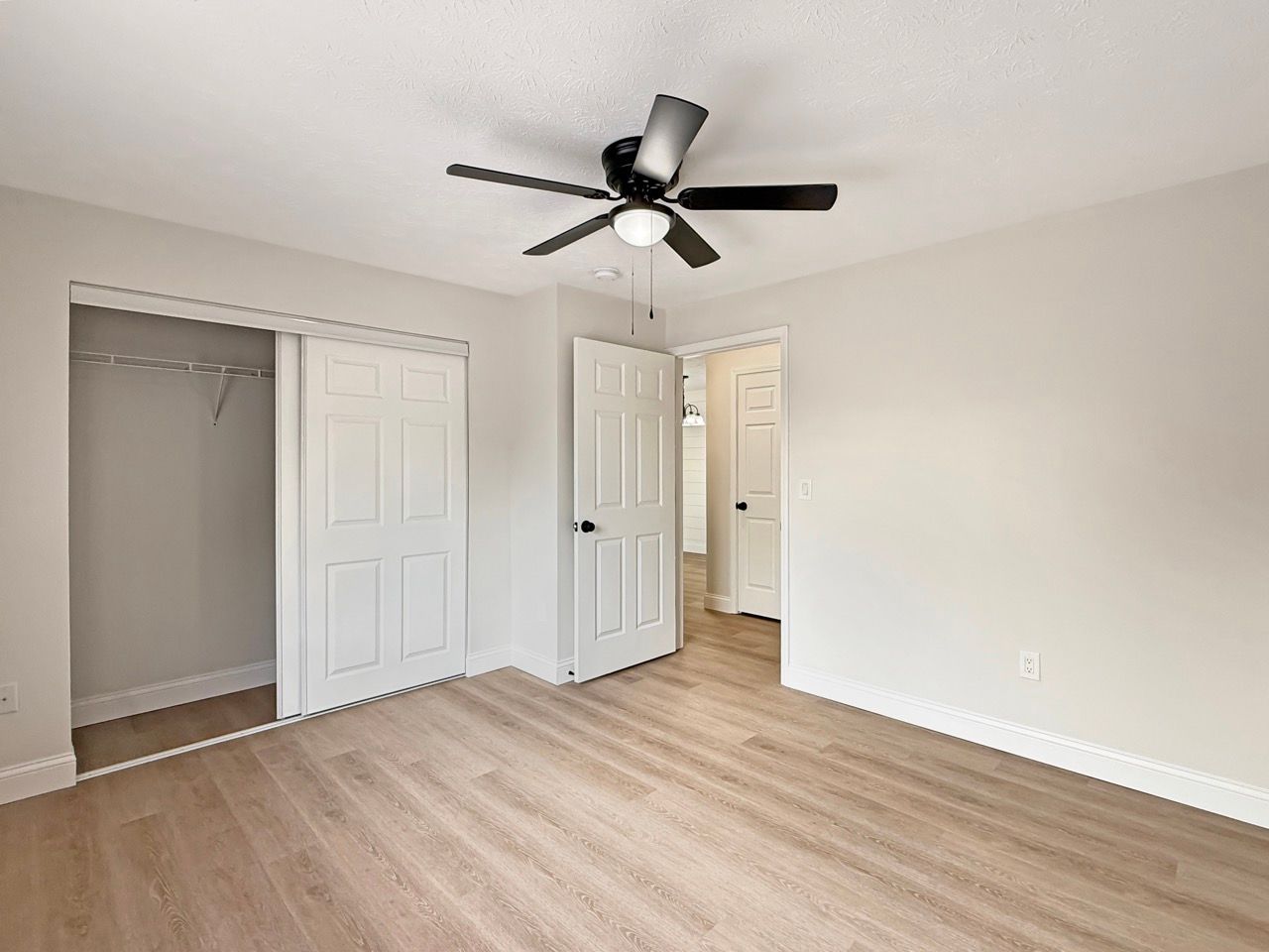 Empty bedroom with light wood floors, open closet, white doors, and ceiling fan.