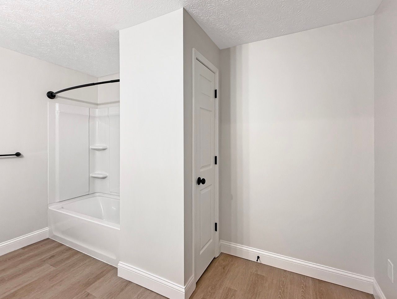 Empty white bedroom with a small closet nook and wood flooring, viewed from the corner