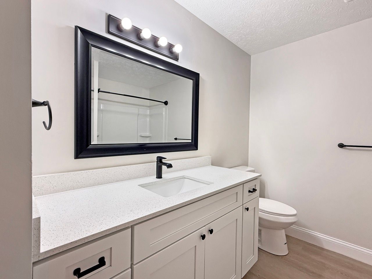 Modern bathroom with white vanity, black-framed mirror, and toilet under gray walls