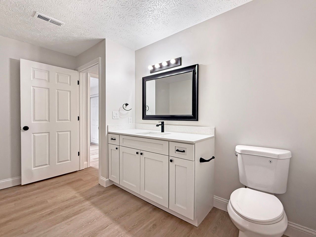 Bright bathroom with white vanity, black mirror, toilet, and light wood floor