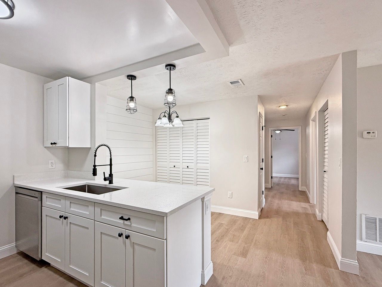 Modern white kitchen with island, pendant lights, and hallway leading to another room