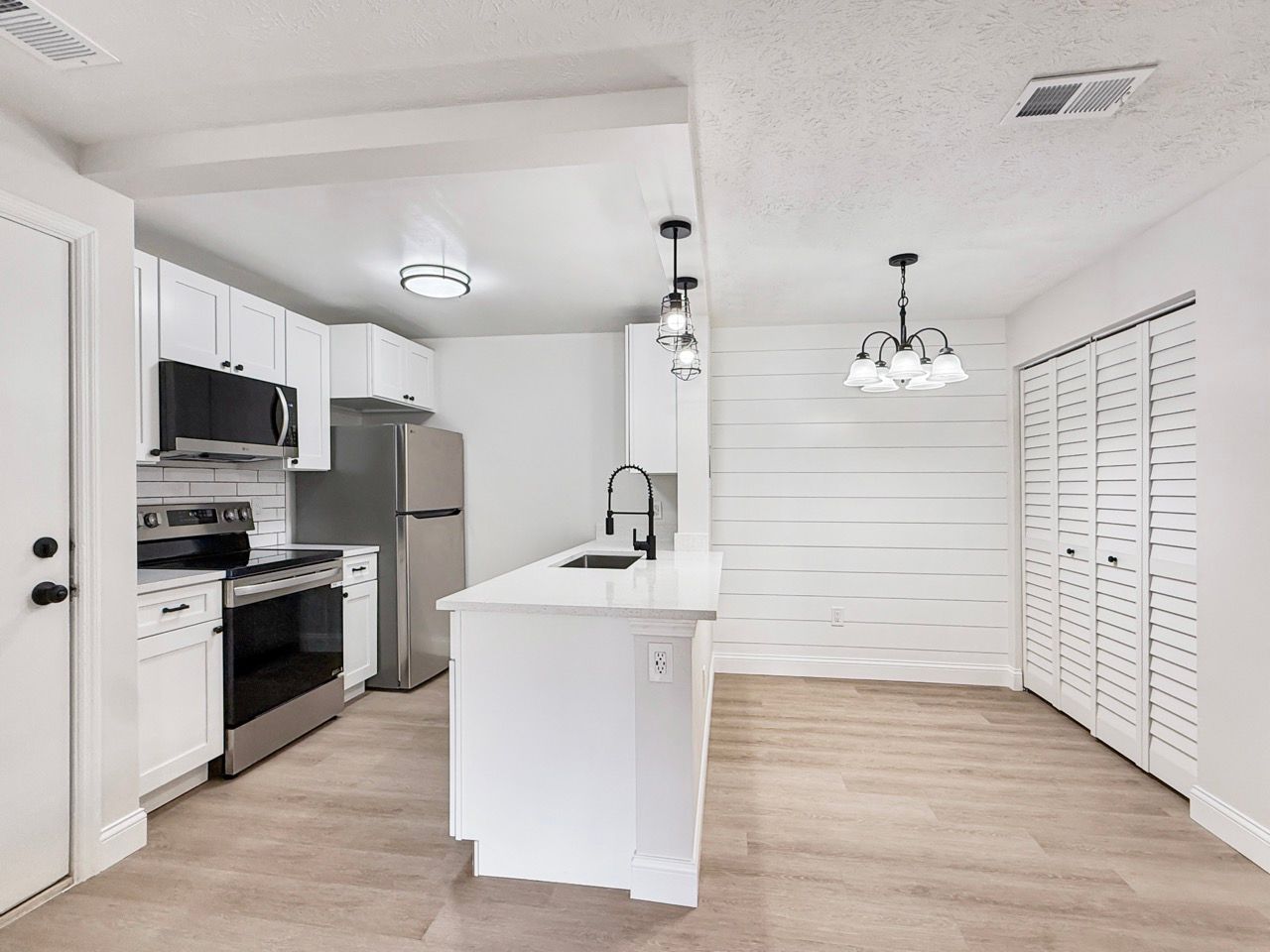 Bright modern kitchen with white cabinets, island, stainless appliances, and wood-look flooring
