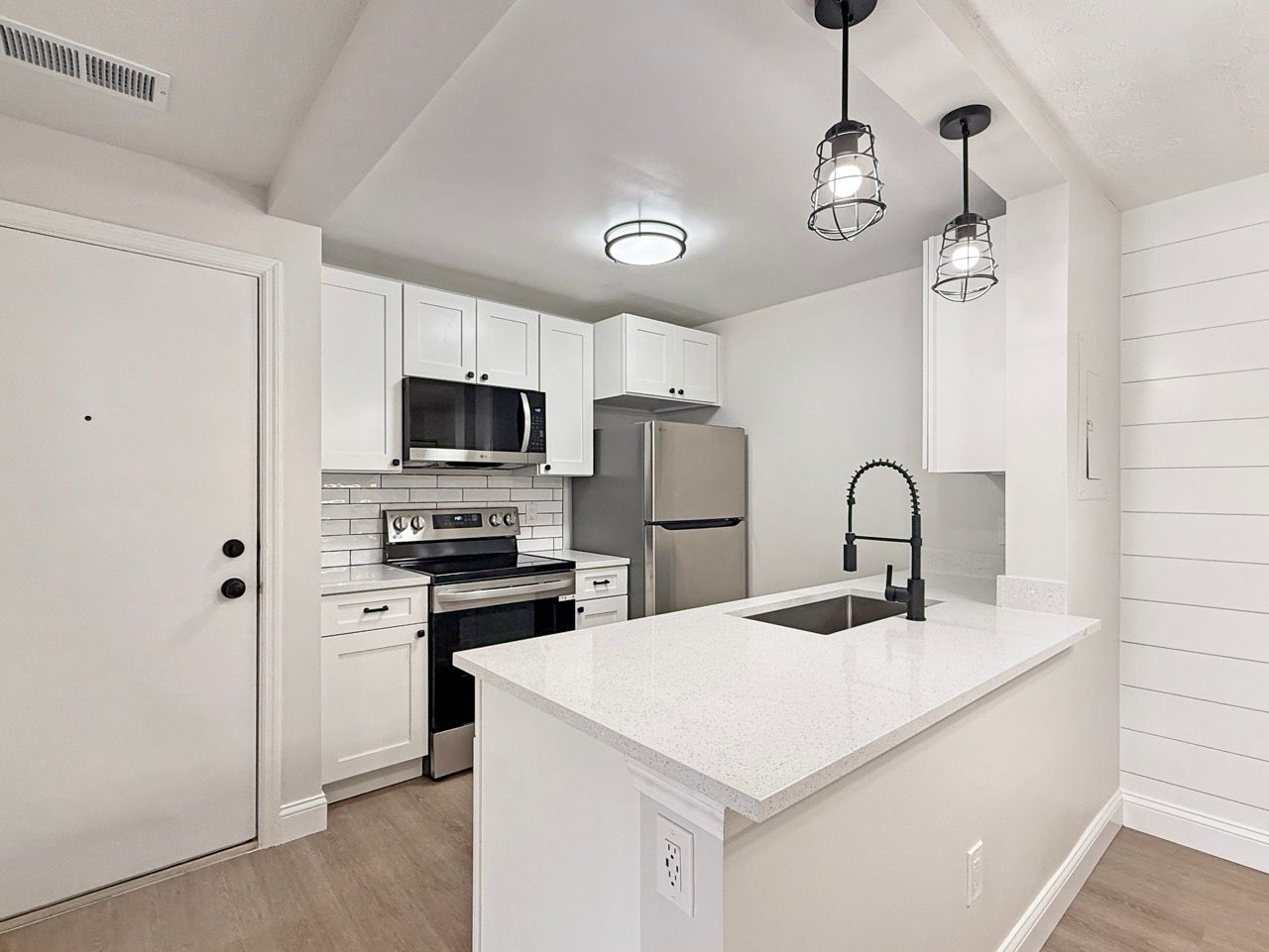 Modern white kitchen with island, stainless steel appliances, pendant lights, and bar stool.