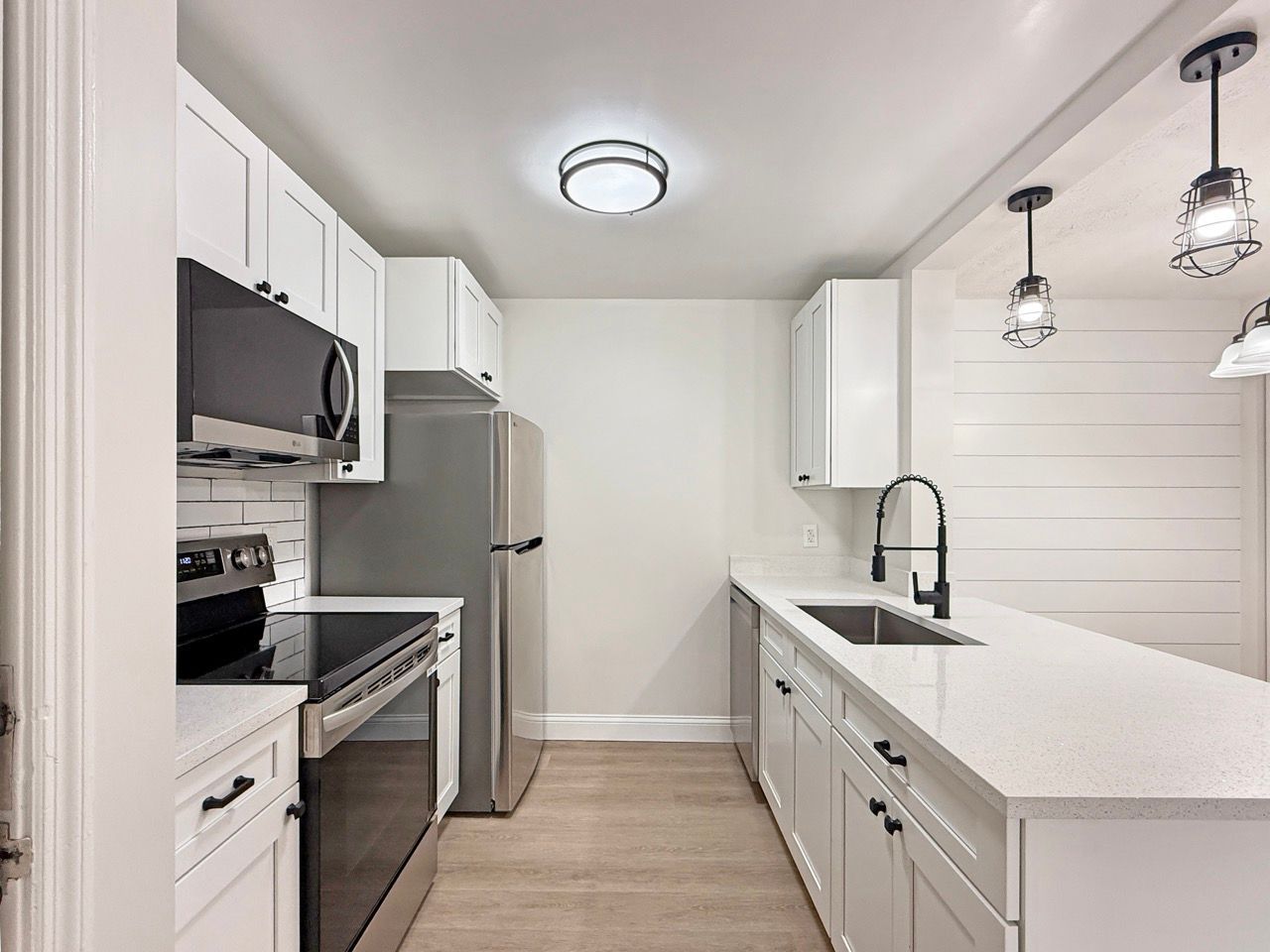 Bright modern kitchen with white cabinets, stainless appliances, and a large island with pendant lights.