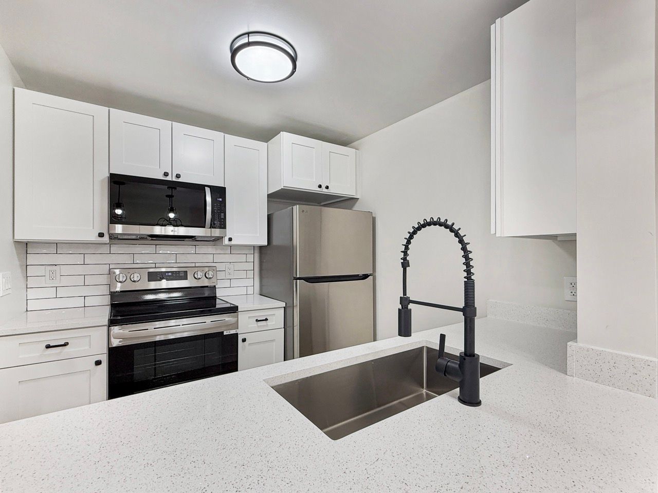 Modern white kitchen with stainless steel appliances, black faucet, and white countertop island