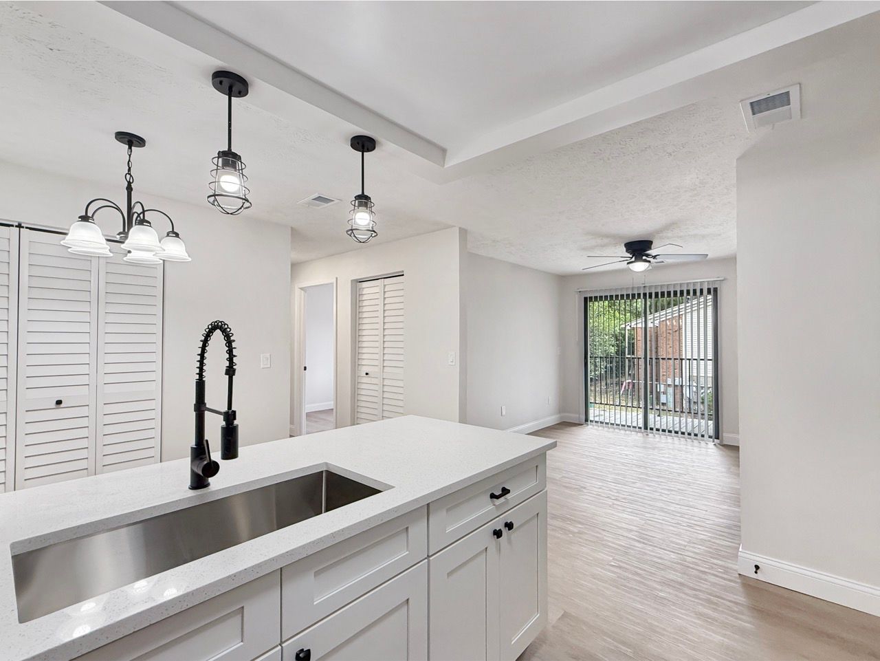 Bright white kitchen with island sink, pendant lights, and sliding doors to a patio