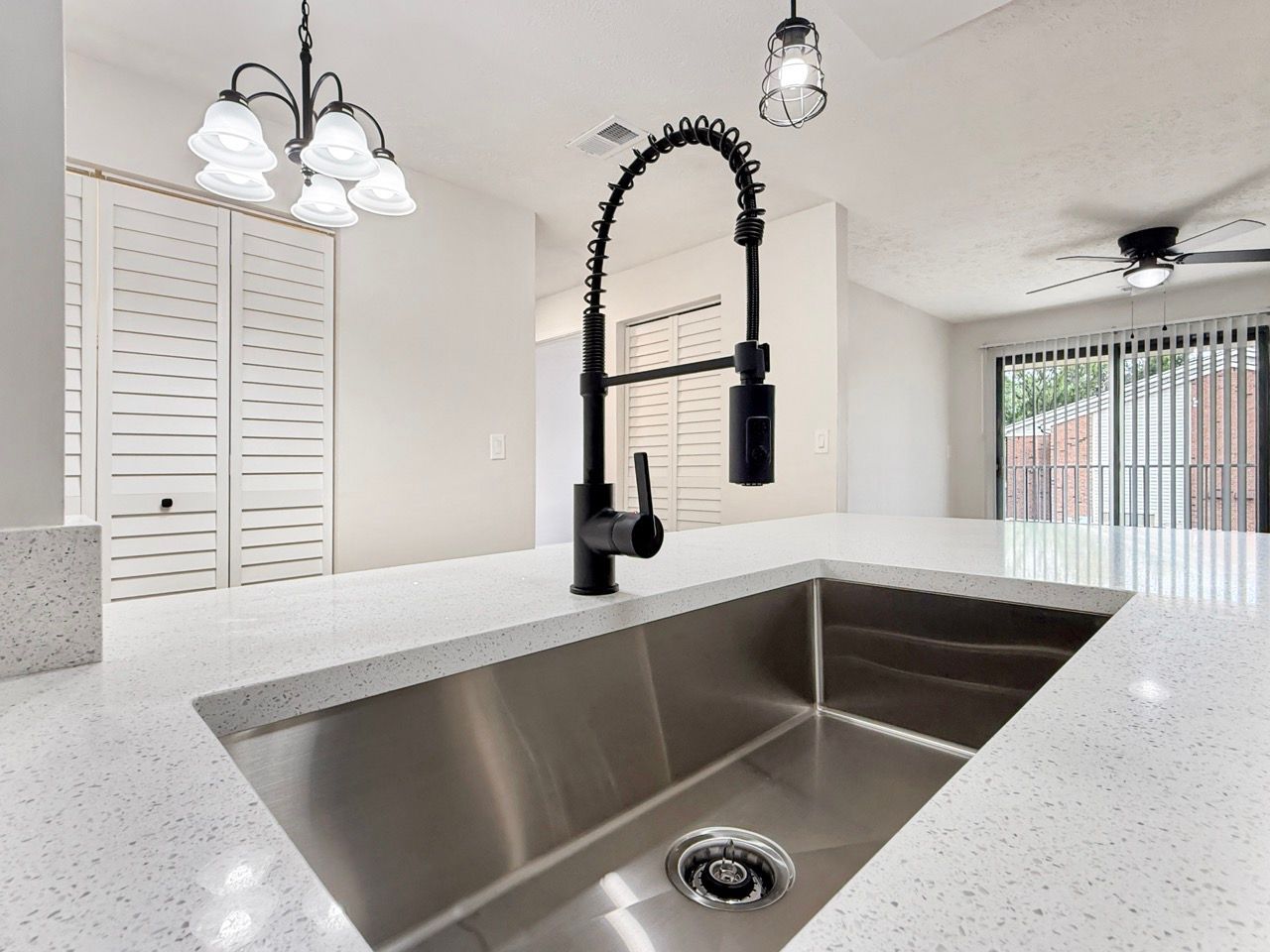 Bright kitchen with a large stainless-steel sink, white quartz island, black faucet, and pendant lights.