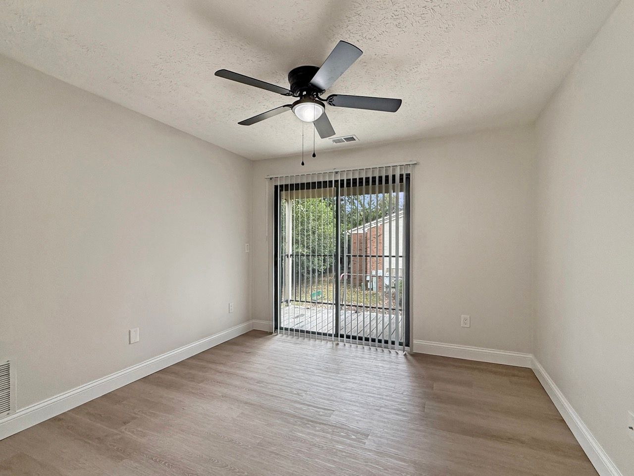 Empty white living room with ceiling fan and sliding glass door with vertical blinds.