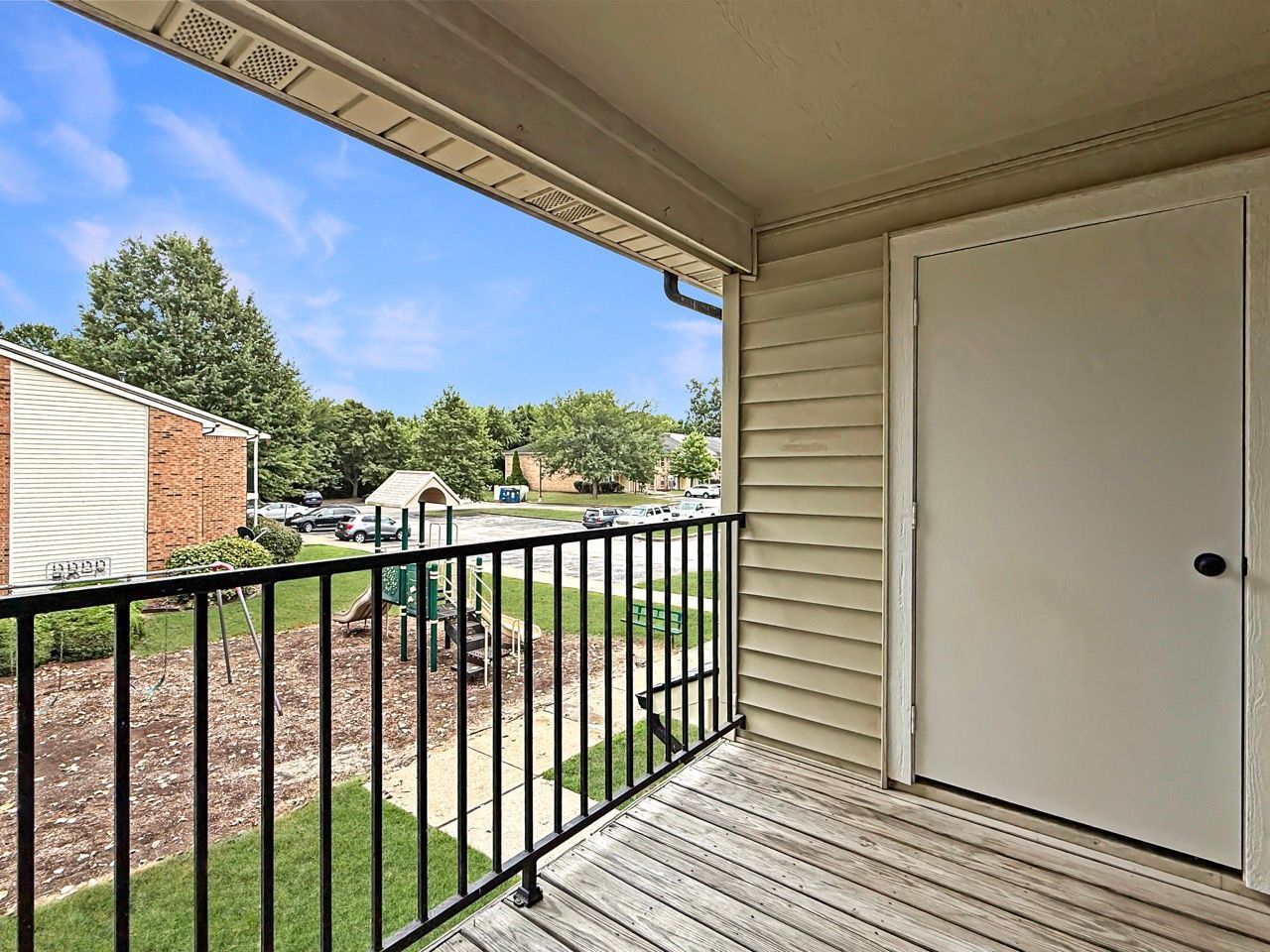 Covered porch with beige siding, black railing, and white storage door overlooking a grassy courtyard.