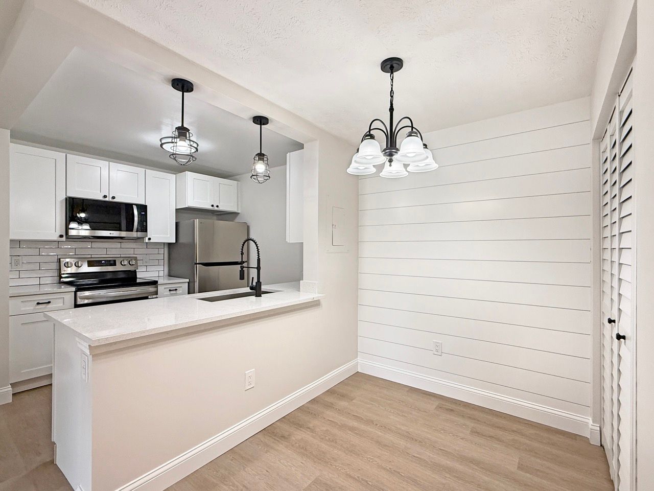 Bright kitchen with white cabinets, stainless appliances, pendant lights, and a dining nook with shiplap wall