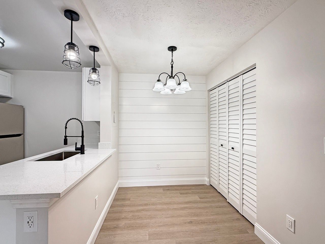 Bright kitchen with white cabinets, granite island, pendant lights, and wood-look flooring