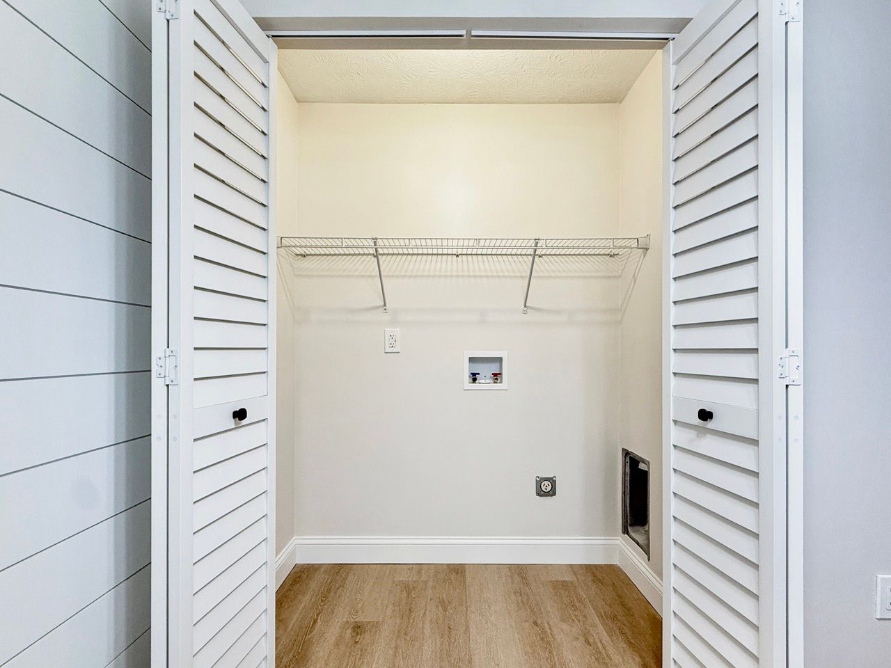 Empty laundry closet with white bi-fold doors, wire shelving, and wood flooring.