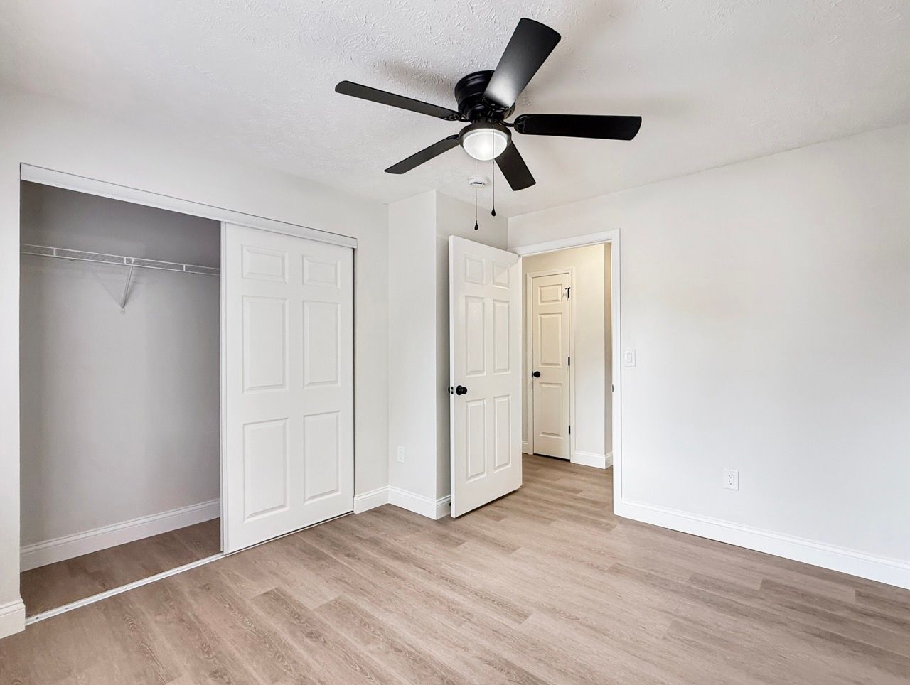 Empty white bedroom with open closet, ceiling fan, and wood-look flooring