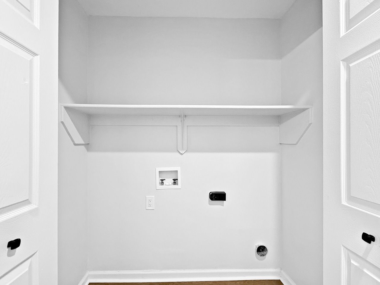 Empty white closet with shelves, hanging rod, and utility hookups on the back wall