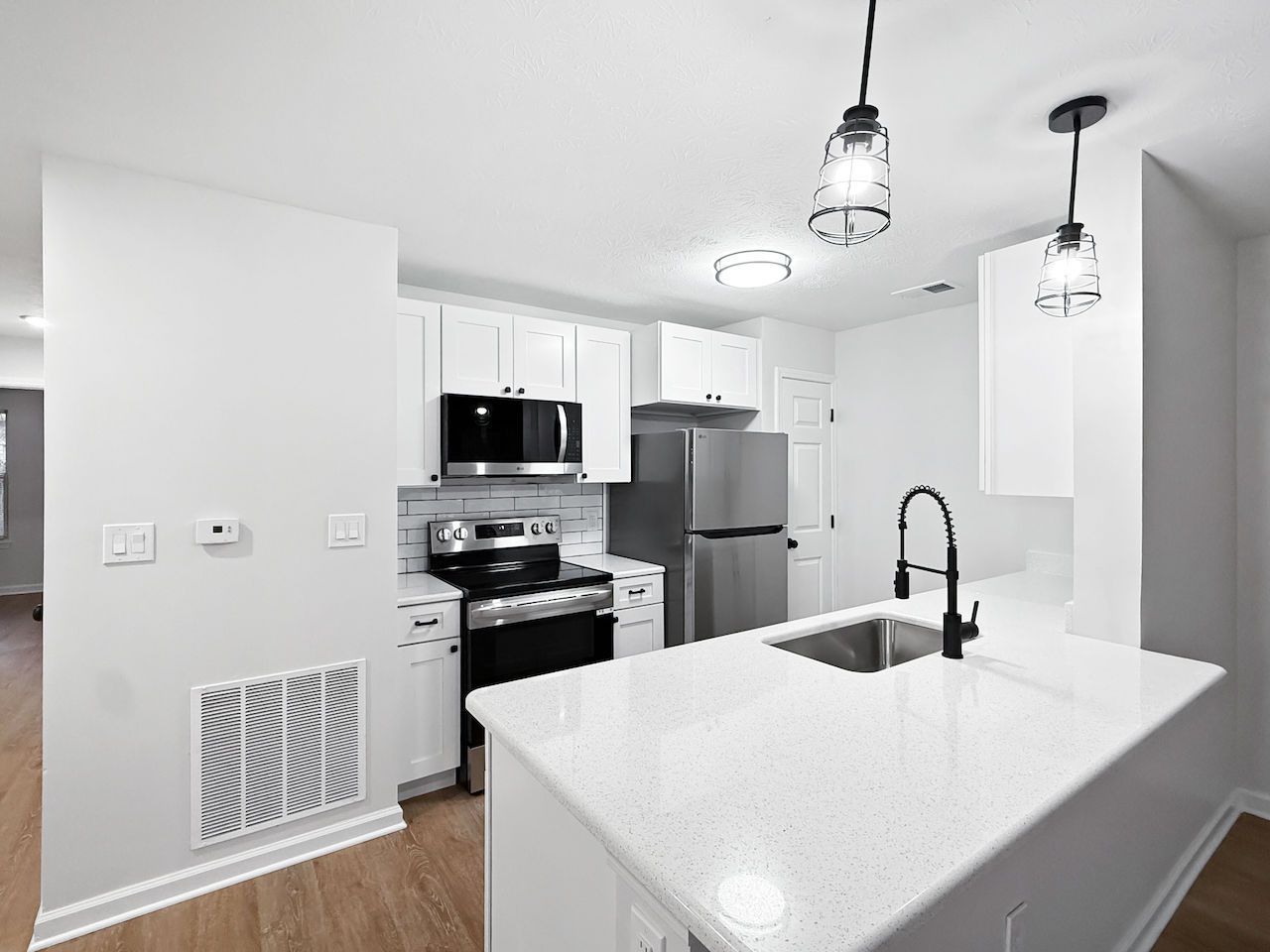 Bright modern kitchen with white island, black fixtures, stainless appliances, and hanging pendant lights.