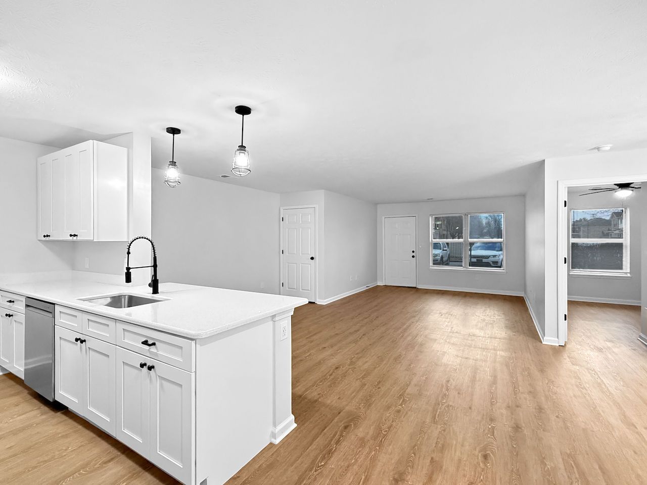 Bright open kitchen and living area with white cabinets, island, and wood floors, lit by pendant lights.
