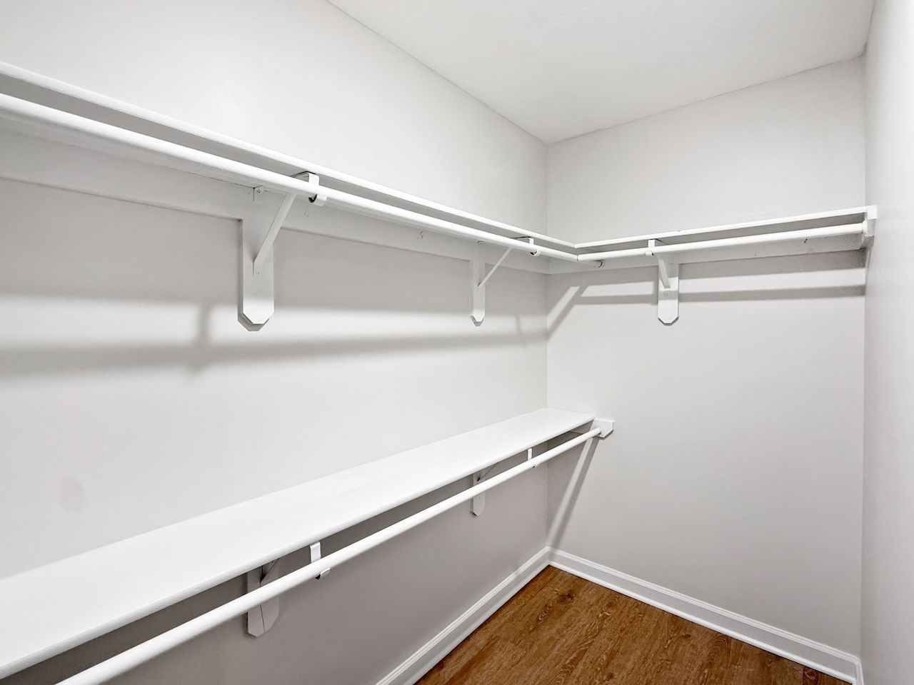 Empty white walk-in closet with wire shelving and hanging rods along two walls, and a wood floor.