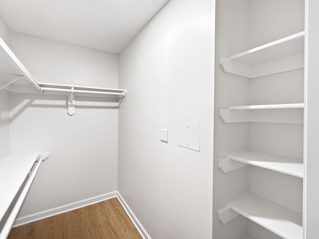Empty white walk-in closet with shelves, hanging rods, and wood flooring