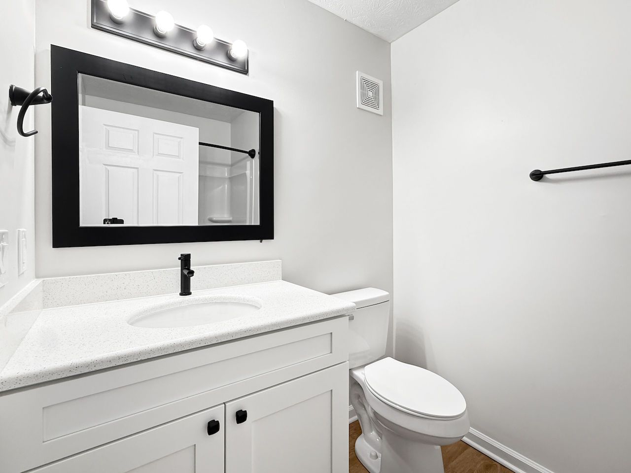 Bright white bathroom with vanity, mirror, sink, toilet, and towel bar.