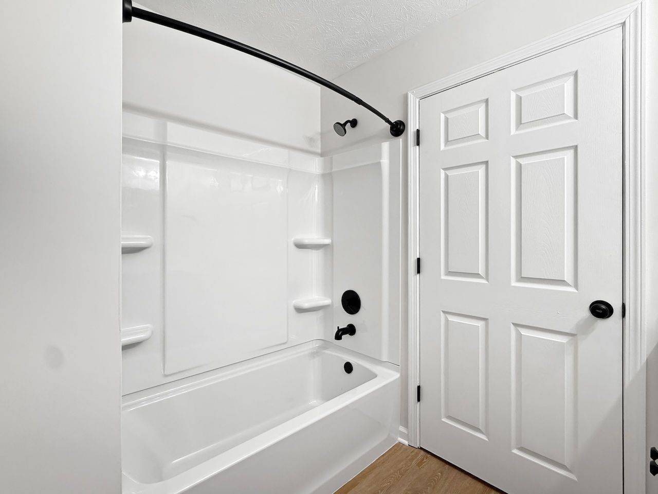 Bathroom with white tub, shower, and door in a bright, clean interior