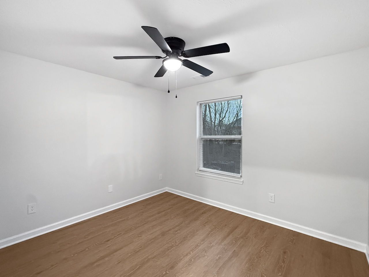 Empty white bedroom with wood floor, ceiling fan, and a small window with blinds