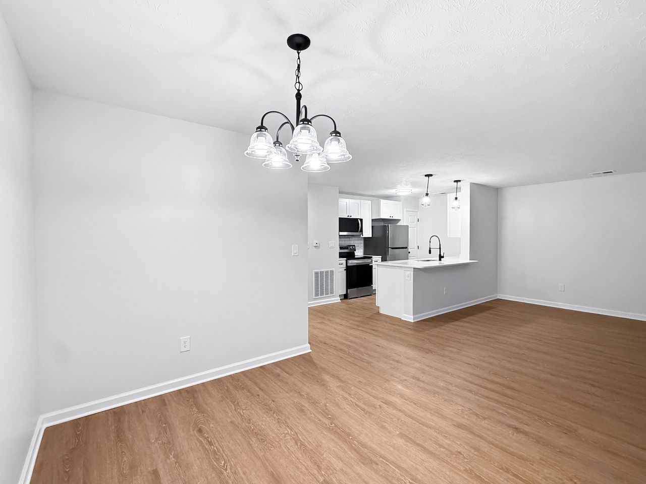 Empty living/dining room with wood floors, white walls, and a kitchen pass-through.