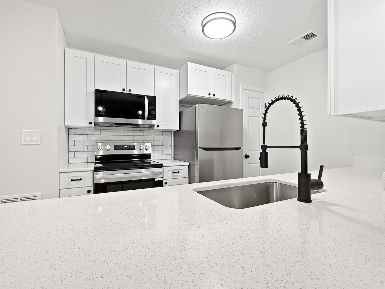 Bright modern white kitchen with stainless steel appliances, speckled island, and black faucet