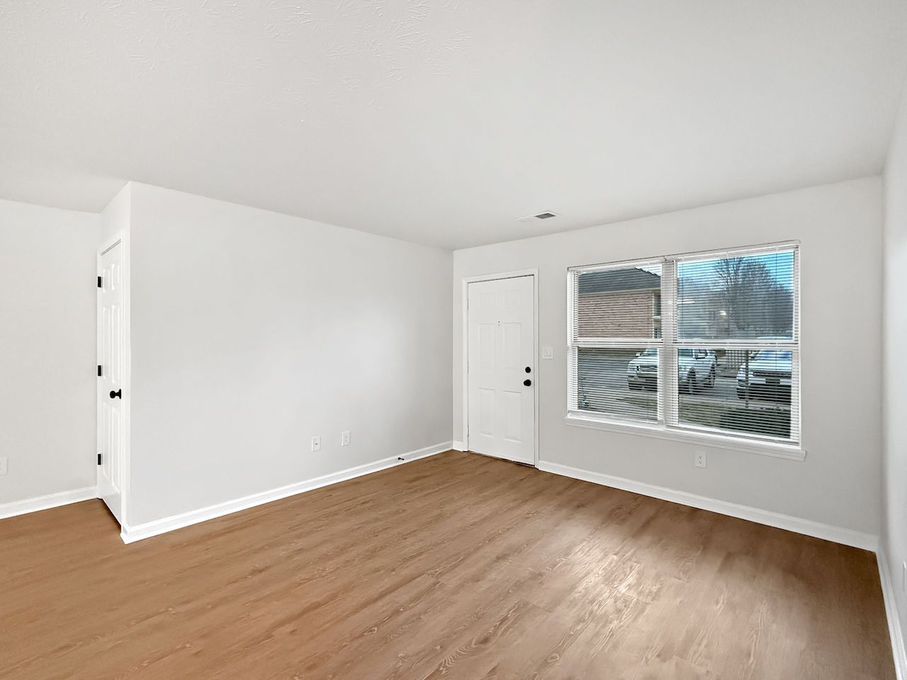 Empty white room with wood floors, a window, and a closed door