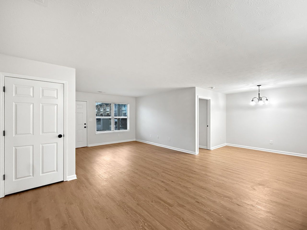Empty unfurnished living room with light wood floors, white walls, and a window.