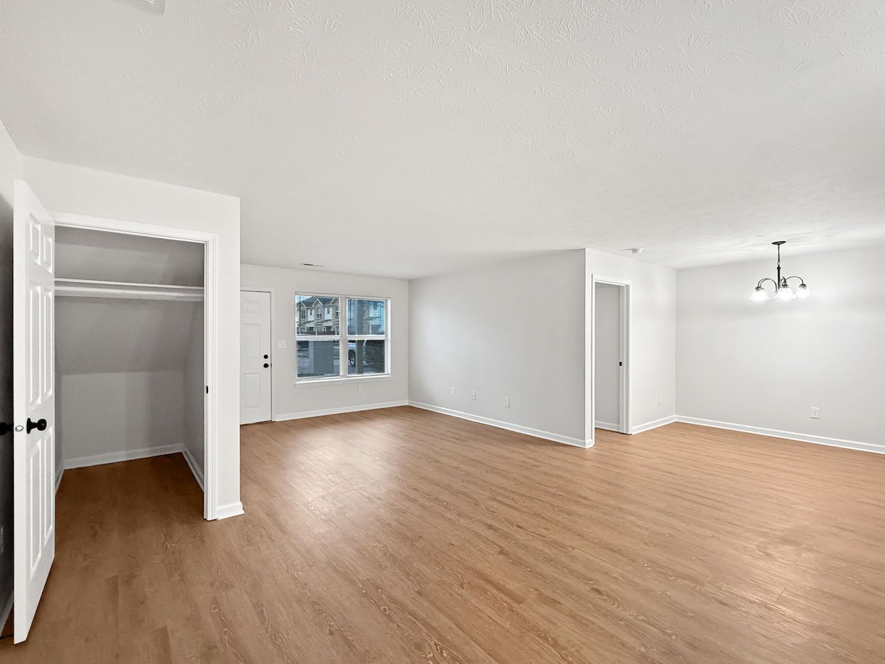 Empty bright living room with wood floors, open closet, and white walls near a window.