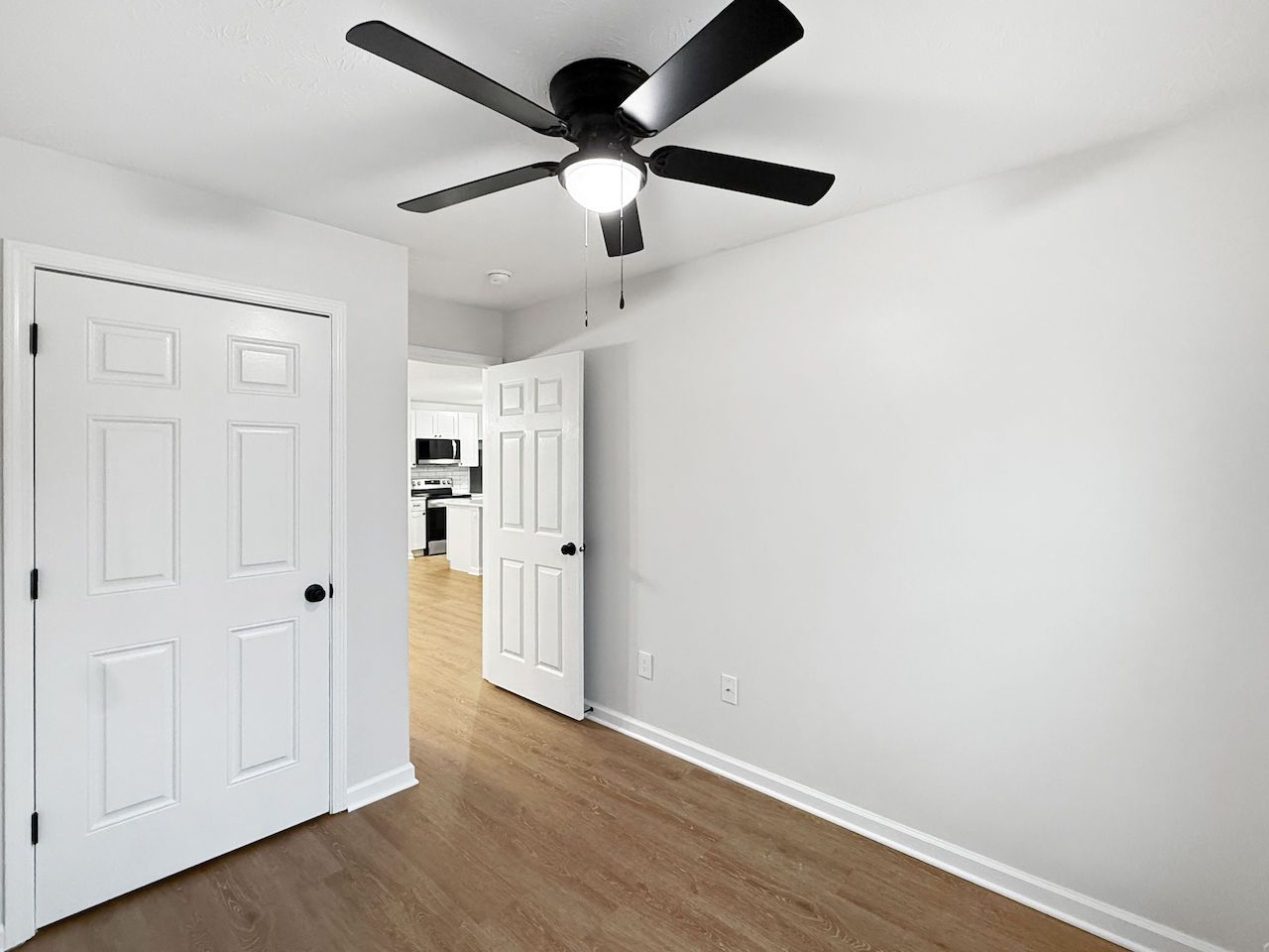 Empty white room with wood floors, white double doors, and a black ceiling fan.