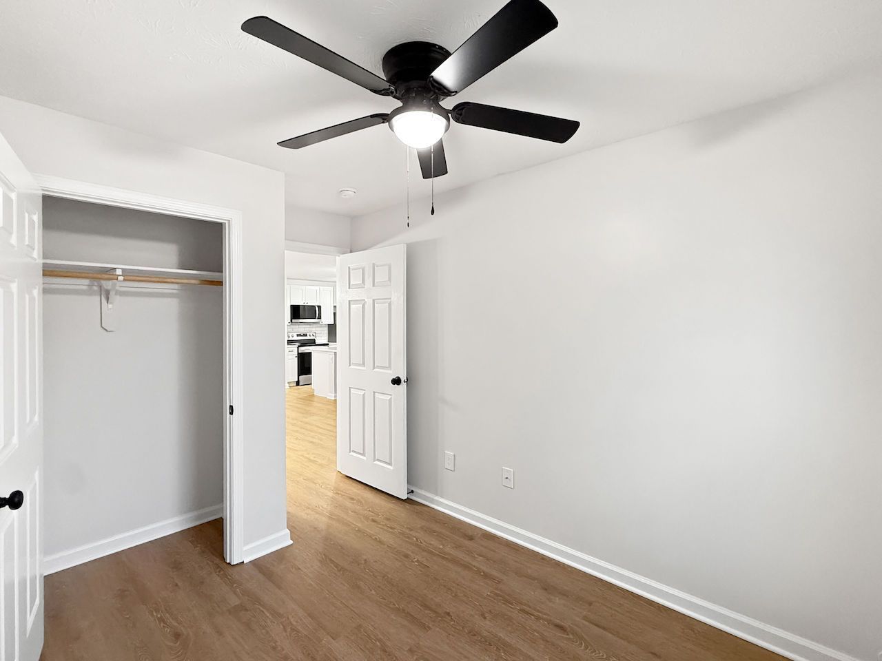 Empty white bedroom with wood floor, open closet, and black ceiling fan on a white ceiling.
