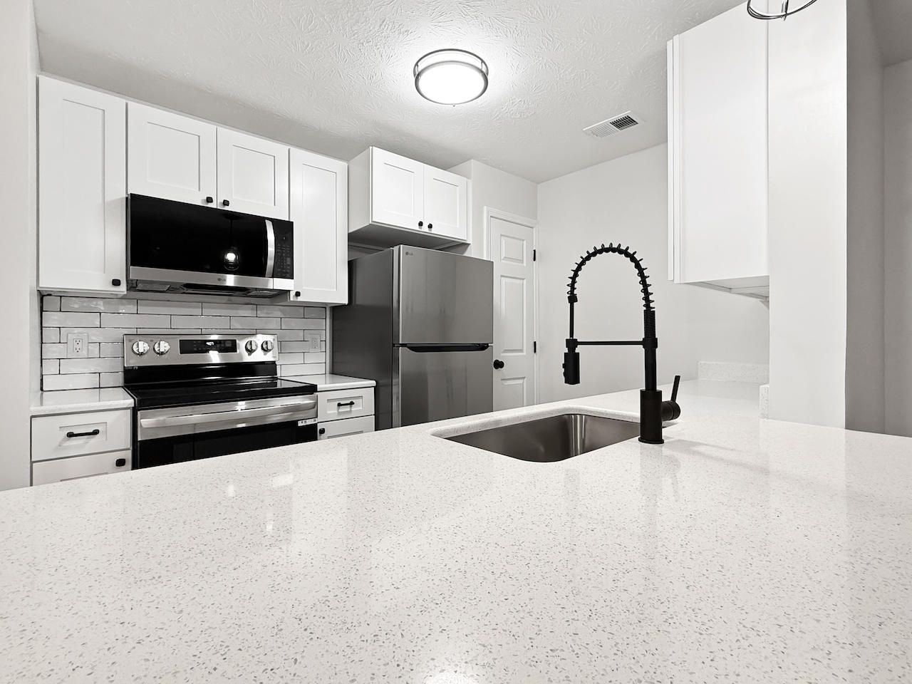 Bright white modern kitchen with stainless steel appliances and a large island sink.
