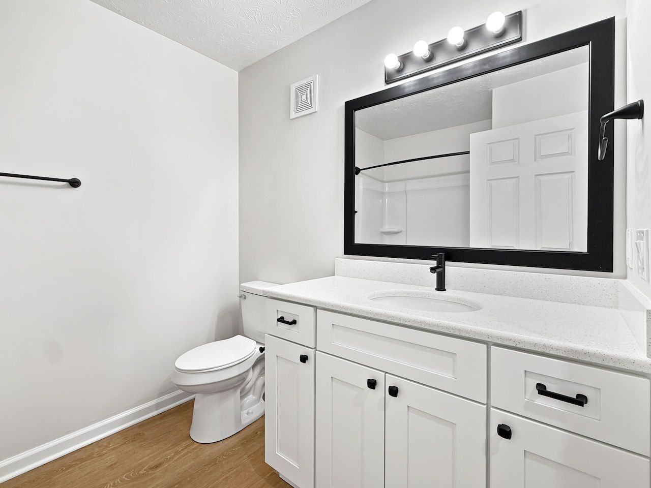 Modern bathroom with white vanity, large mirror, and toilet near a towel bar.