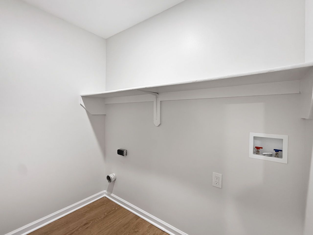 Empty white laundry room with a shelf, wall hookups, and wood floor