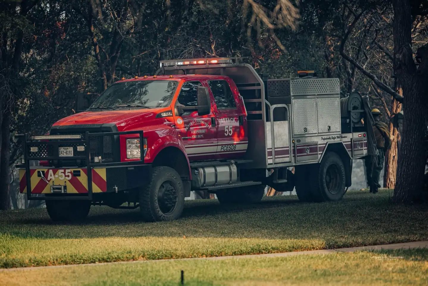 Red fire truck parked on grass beside trees, with equipment compartments and a ladder on top