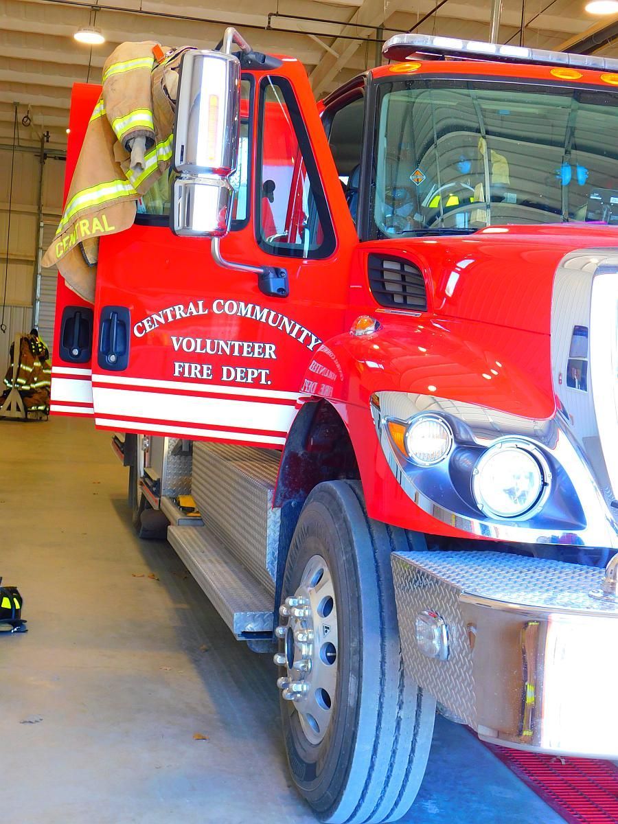 Red fire truck parked in a station bay, viewed from the front side with reflective lettering.