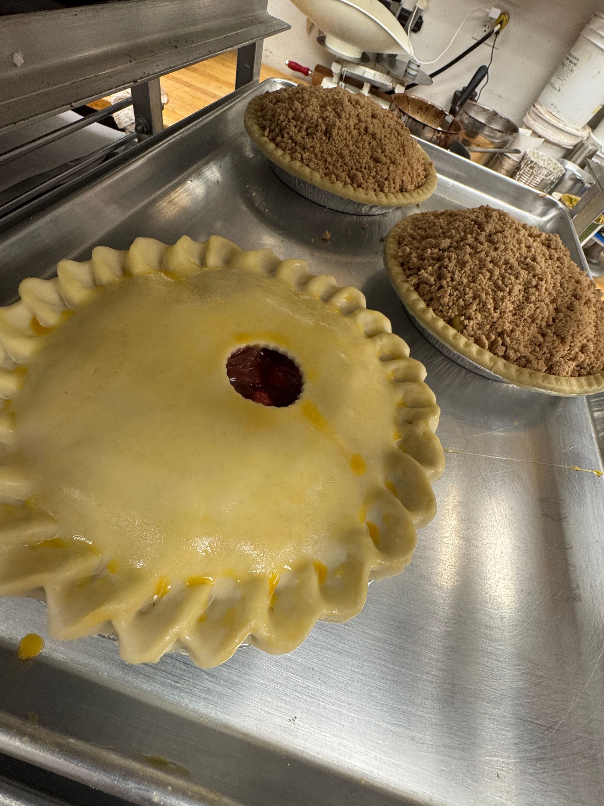 Three pies on a metal tray. One with a top crust and a hole, two with crumb topping.