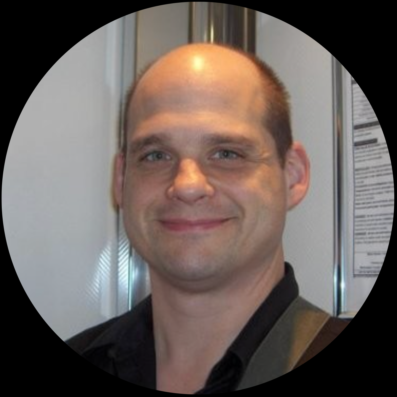 Smiling bald man in a black shirt, photographed inside a light-colored setting.