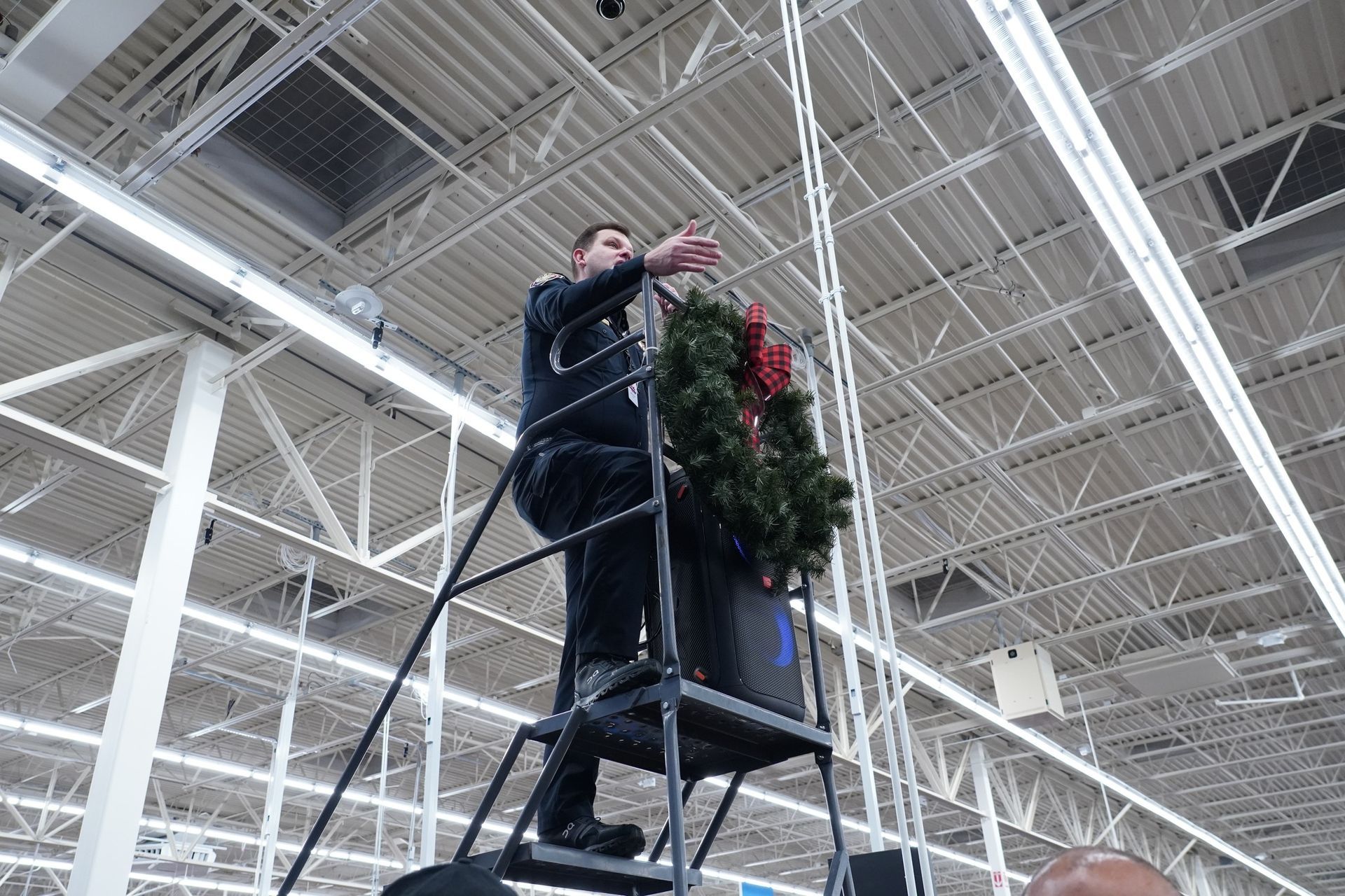 A man is standing on a ladder holding a christmas wreath.