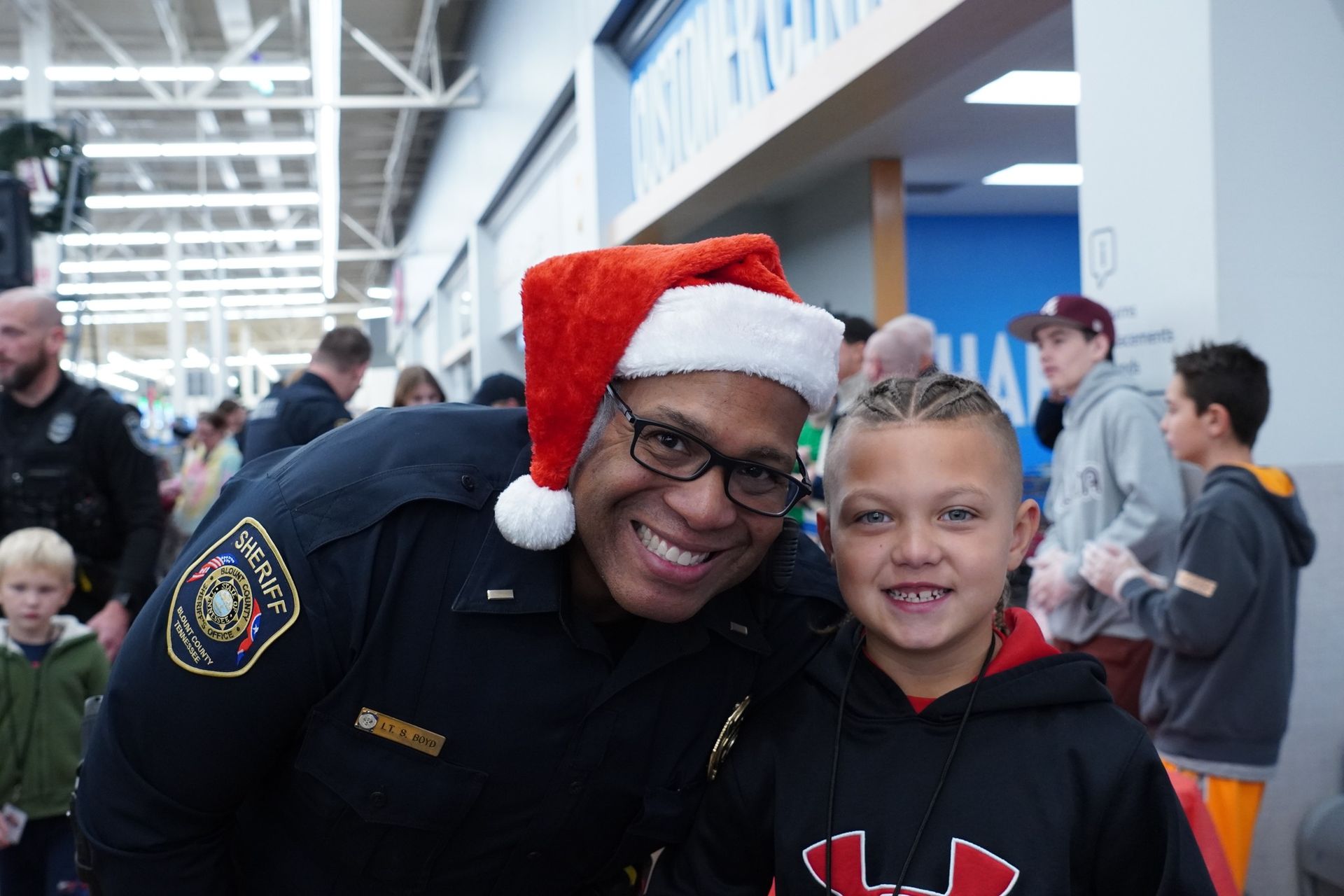 A police officer wearing a santa hat is posing for a picture with a young boy.